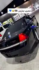 A sleek black car is shown being refueled at a gas station at night. A text overlay in Arabic reads 'نجب بنزين 98' (We love 98 octane fuel), accompanied by heart and smiling face emojis. The scene captures the modern, clean aesthetic of a luxury vehicle receiving premium fuel, highlighting a moment of care and performance for the owner. by @kfl1 with عب فول لاشري المحطه كلها⛽️. by Sn: K F L 1