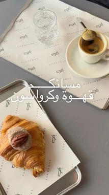 This video captures a serene morning coffee moment. It opens with a beautifully styled flat lay of a croissant topped with a pecan and cream, served on branded Sequence Coffee paper. Next to it sits a small espresso cup with a spoon, ready to stir, and a glass of water on a matching tray. The scene is calm and inviting, showcasing a simple yet elegant café experience. Arabic text overlays 'مُسَائِكُمْ قهوة و كرواسون' (Good morning, coffee and croissant), enhancing the welcoming theme. This visual is ideal for anyone searching for coffee shop aesthetics, morning inspiration, or branding ideas. by @sequence-coffee with original sound