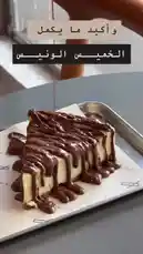 A close-up shot captures a rich slice of cheesecake being generously drizzled with melted chocolate sauce. The text overlay in Arabic reads 'And what more delicious than cheesecake?'. This visually appealing moment highlights the decadence of the dessert. by @sequence-coffee with Original Sound by sequence-coffee