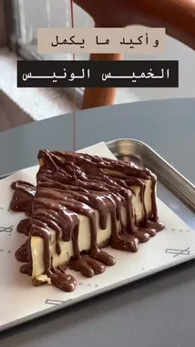 A close-up shot captures a rich slice of cheesecake being generously drizzled with melted chocolate sauce. The text overlay in Arabic reads 'And what more delicious than cheesecake?'. This visually appealing moment highlights the decadence of the dessert. by @sequence-coffee with Original Sound by sequence-coffee