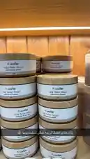 This close-up video showcases stacks of 'Herb and Oil Taberna' body butter jars, highlighting their elegant wooden lids and minimalist design. A text overlay in Arabic promotes the product as a natural skincare solution. The warm lighting and wooden background create an inviting atmosphere, emphasizing the brand's focus on organic ingredients and traditional wellness. by @ru.ab71 with original sound