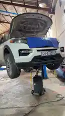 This video shows a white SUV being lifted by a hydraulic jack in a garage setting. The hood is open, suggesting maintenance or repair work. A blue tarp covers part of the front bumper, possibly protecting it during service. The vehicle is positioned on a sturdy lift, highlighting proper safety procedures for automotive work. by @hawkar_service with original sound