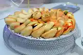 A beautifully arranged assortment of golden-brown pastries fills a decorative silver mesh serving tray. Each pastry appears freshly baked, with some filled with savory ingredients like olives and cheese, while others are plain or topped with herbs. The setting suggests a catering event, party appetizer display, or elegant brunch gathering. The visual focus is on the appealing textures and variety of the pastries, highlighting their craftsmanship and presentation. by @blue11sweet with original sound