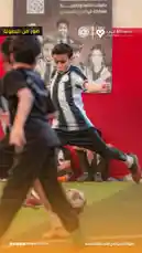 في هذا الفيديو، نرى لاعبًا شابًا يتدرب على مهارات التحكم بالكرة داخل صالة رياضية. يرتدي اللاعب قميصًا بخطوط بيضاء وسوداء، ويظهر تركيزه الشديد أثناء تنفيذ حركة تمرير أو تسديد. في الخلفية، يجلس أطفال آخرون يتابعون التدريب، بينما يعلق على الحائط ملصق إعلاني يحمل شعار جمعية اللاعب والرسالة: 'بطولات داخلية وخارجية مشاركة في الدوري السعودي'. يشير النص 'صور من البطولة' إلى أن هذا المحتوى جزء من تغطية رسمية لحدث رياضي. يعكس المشهد روح التنافس والتدريب المهني في بيئة رياضية مخصصة للأطفال. by @playerassoc with original sound