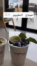 A close-up view of a beautifully presented dark blue drink from Sequence Coffee, garnished with fresh mint and a lemon slice. The modern café setting features stylish furniture and large windows, creating an inviting atmosphere. An Arabic text overlay reading 'صباح الخير' (Good morning) adds a warm, welcoming touch. by @sequence-coffee with Life sound🪷🌱 by 🌺✨🐚💗