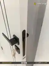 A close-up view of a sleek, black modern door handle being installed on a white door. A key is inserted into the lock cylinder, demonstrating the hardware's functionality. The branding 'الهيكل الثابت للمقاولات' is visible in the corner, indicating the contractor specializing in construction and installations. by @fixedstructure with original sound