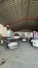 This behind-the-scenes look at Wasta Hawkar's auto repair facility shows mechanics working on vehicles under a large industrial roof. A silver SUV is being serviced with its hood open, while other cars wait nearby. Workers move around the garage, highlighting the daily operations of a busy auto service center. The setting features prominent Liqui Moly branding, suggesting a focus on quality maintenance and lubricants. by @hawkar_service with original sound