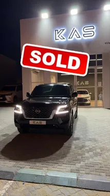 A sleek black Nissan Patrol SUV is showcased in front of the illuminated 'KAS' dealership at night. A large red 'SOLD' graphic is overlaid on the screen, indicating a successful sale. The vehicle's headlights are on, highlighting its modern design against the dark backdrop. by @aaaaaa with كاريزما عاليه by '