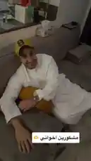 In this heartwarming moment, Mohammed Al-Omair, wearing a white thobe and a yellow cap, is surprised by his friends during what appears to be a birthday celebration. He is initially seen relaxing on a couch before being presented with a cake adorned with a lit candle. His friends, also dressed in traditional attire, gather around him, capturing the joyful surprise on their phones. The scene captures a genuine moment of friendship and celebration. by @bbbbb with Happy Birthday (Piano Version) by Magical Tunes