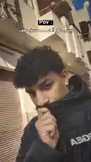 This short-form video opens with a young man in a black jacket looking pensive against a backdrop of a building. Text overlay reads 'Pov: أحسين ملك' (Pov: I feel like a king). The scene then cuts to a striking black-and-white image of a cheetah sitting calmly inside a stable, while a greyhound sprints past it at full speed, kicking up dust. The contrast between the majestic predator's stillness and the racer's blur of motion creates a surreal and humorous POV moment. by @sofaa_66 with sofaa_66 by Original Sound