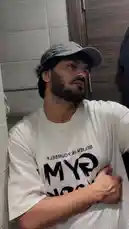 A young man, identified as D SUN, poses confidently in a white mesh t-shirt with 'BELIEVE IN YOURSELF' and 'GYM' printed on it, along with a grey baseball cap. He stands in what appears to be a gym locker room or changing area. The scene is accompanied by a soulful, melancholic song in Hindi/Urdu, creating a reflective and motivational atmosphere. by @dsunmusic with Laaya by Mitraz