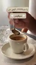 A close-up shot shows a hand using a small spoon to stir espresso in a white cup, demonstrating the ideal technique for mixing coffee grounds and water. This simple yet crucial step is essential for achieving the perfect crema and flavor in your espresso. The setting appears to be a cozy café, emphasizing the art of coffee preparation. by @sequence-coffee with موسيقى محمد عبده🖤🎶 by 🎶