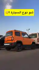 A vibrant orange off-road SUV is displayed in a desert parking lot under a clear blue sky. The vehicle features rugged tires, black trim, roof rails, and a modern boxy design. This static shot highlights the SUV's bold aesthetic and off-road capabilities. by @aaaaaa with يالله القتقوتي😋😂🤏🏻 by ٰ