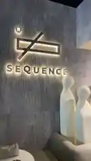 This video offers a glimpse into the stylish interior of Sequence Coffee. The camera pans across a modern space featuring a prominent illuminated logo on a textured wall, complemented by unique white sculptural figures and contemporary furniture, showcasing the brand's sophisticated design. by @sequence-coffee with هذا هووو🤩 by Al3be