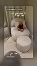 This stylish home corner features a plush, light-colored armchair and matching ottoman, creating a cozy reading nook. A charming teddy bear in a red sweater sits invitingly on the chair. The space is enhanced by a full-length mirror with a gold frame and soft beige curtains. Arabic text overlays express gratitude to Allah and credit the furniture to '@aaththy1'. This serene setup is perfect for anyone looking to create a peaceful and aesthetically pleasing corner in their home. by @aththy1 with Original Sound by aththy1