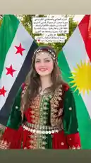 A young woman, identified as Rawan Naser, stands proudly in front of the flags of Syria and the Kurdistan Region. She is wearing an elaborate traditional Kurdish dress, rich in red and green velvet with intricate gold embroidery and a decorative silver belt. A matching headdress completes her festive look. An Arabic text overlay expresses pride in her heritage, wishing prosperity for the Kurdish people and their homeland. by @mediarawan with ريزان بكر _ اجمل اغاني دبكات كردية عربية by Rinas Hussein